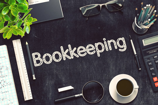 A desk setup with the word 'Bookkeeping' written in a bold, textured font on a black chalkboard-style surface, surrounded by office items including a calculator, glasses, coffee cup, pens, ruler, notepad, and a plant, symbolizing organization and financial management