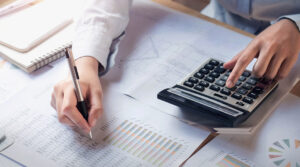 A person reviewing financial documents, using a calculator and pen to analyze charts and data at a desk.